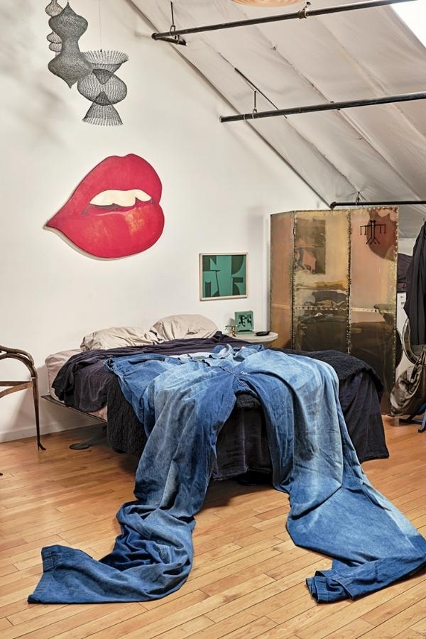 A lip painting after Tom Wesselmann and a group of hanging wire sculptures after Ruth Asawa hang over a brass-riveted Sarreid- style three-panel room divider and a pair of three-metre vintage Sedgefield jeans on Pessin’s bed. Photography by Philip Cheung.