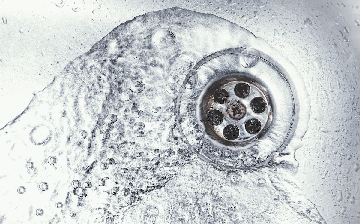 water drain down on stainless steel kitchen sink hole. top view sewer in washbasin. household plumbing. cleaning and hygiene concept.