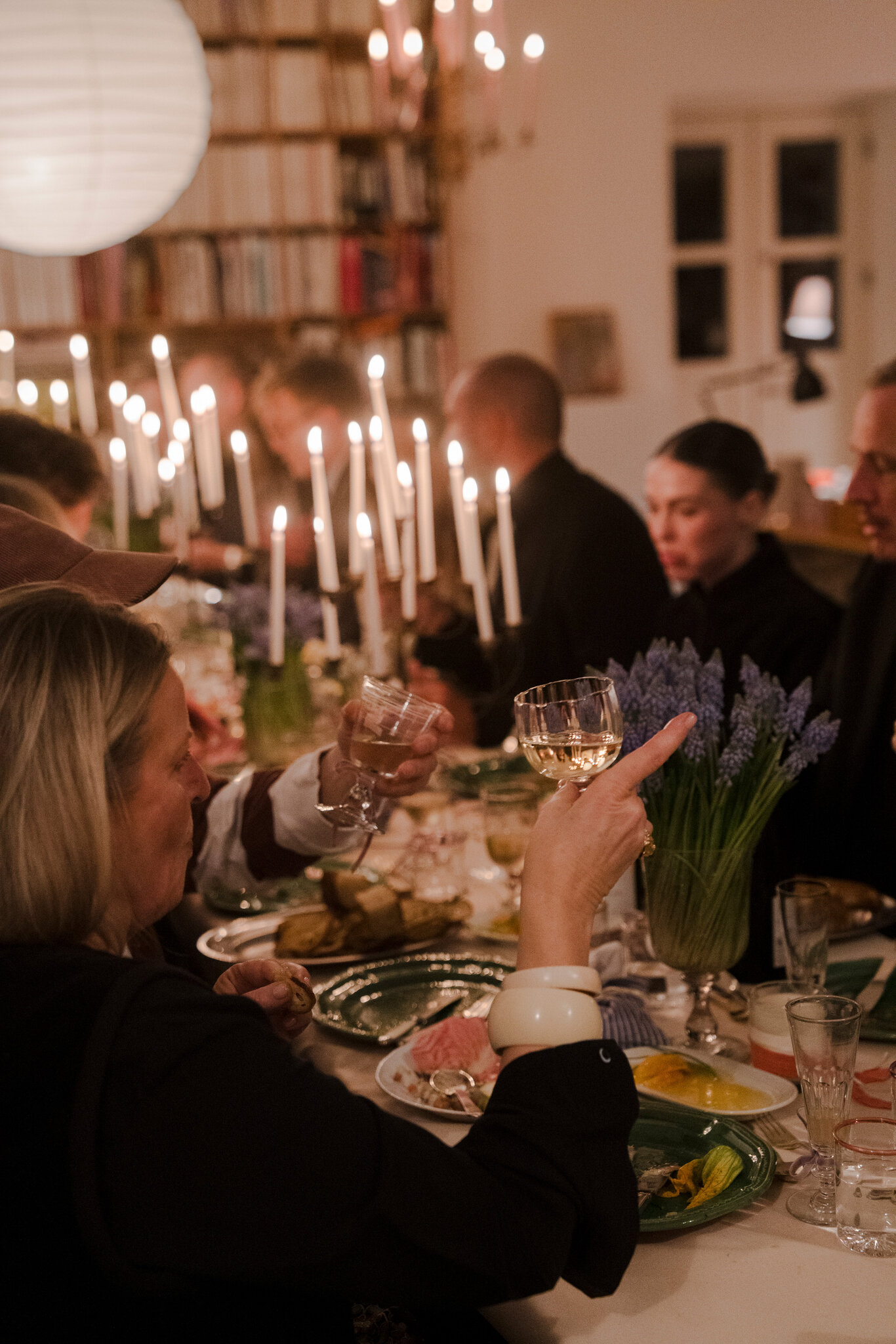 Guests sitting on a long trestle table lit with tall candles.